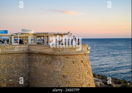 Les personnes qui apprécient la nourriture et les boissons au restaurant en plein air Buena Vista sur le bord de mer médiéval rempart dans la vieille ville de Gallipoli, Apulia (Puglia), Italie. Banque D'Images