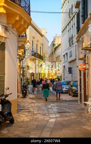 Touristes et habitants marchant le long d'une rue typique étroite et pavée dans la vieille ville de Gallipoli en début de soirée, Apulia (Puglia), Italie. Banque D'Images