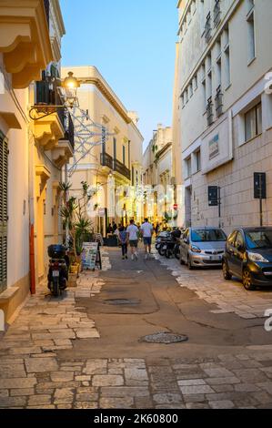 Touristes et habitants marchant le long d'une rue typique étroite et pavée dans la vieille ville de Gallipoli en début de soirée, Apulia (Puglia), Italie. Banque D'Images