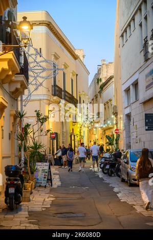 Touristes et habitants marchant le long d'une rue typique étroite et pavée dans la vieille ville de Gallipoli en début de soirée, Apulia (Puglia), Italie. Banque D'Images