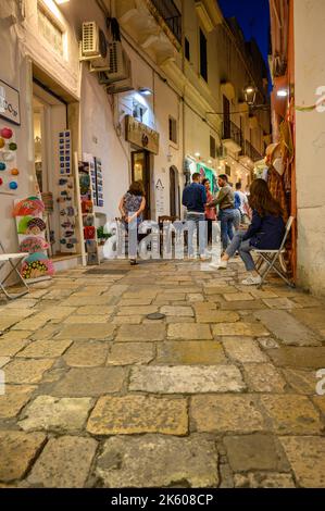 Touristes et habitants marchant le long d'une rue typique étroite et pavée dans la vieille ville de Gallipoli dans la soirée, Apulia (Puglia), Italie. Banque D'Images