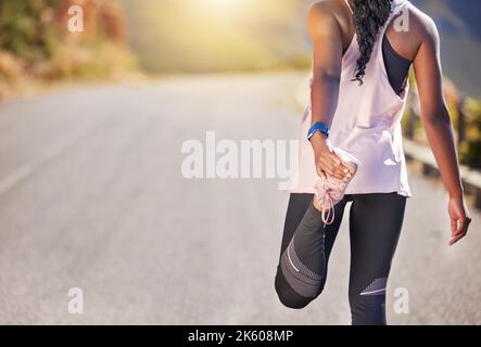 Gros plan sur une athlète afro-américaine qui s'étire avant une course à l'extérieur sur une route. L'exercice est bon pour votre santé et votre bien-être. L'étirement, c'est Banque D'Images