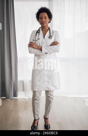 Femme afro-américaine ambitieuse à talons, debout, armée croisée, portant un uniforme. Banque D'Images