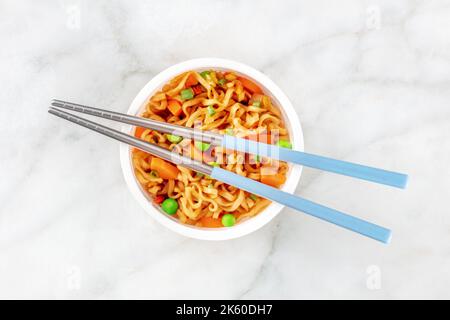 Coupe de ramen, nouilles soba instantanées dans une tasse en plastique avec des légumes, des oignons verts, des pois verts et des carottes, grenaille à plat avec des baguettes Banque D'Images