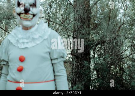 gros plan d'un clown maléfique crépi, portant un costume gris avec pompons rouges et une ruff blanche, en mouvement tandis que se wakling dans les bois au crépuscule Banque D'Images