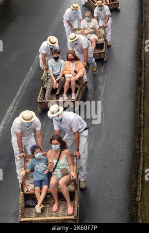 FUNCHAL, PORTUGAL - le 24 AOÛT 2021 : un groupe de touristes non identifiés s'enroulent dans la rue dans des paniers en osier (toboggan) avec l'aide de conducteurs en t Banque D'Images