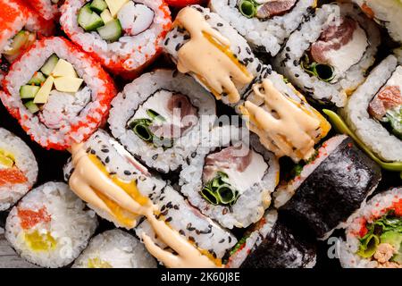 Vue rapprochée de divers petits pains à sushis avec différentes garnitures sur ardoise en métal noir. Sushi au saumon, caviar rouge, fromage, concombre, avocat et se Banque D'Images