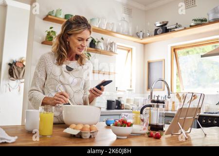 Pâtisserie, site Web et téléphone avec femme cuisant de la nourriture tout en lisant en ligne avec blog, Internet ou app. Cuisine, réseau et petit déjeuner avec chef avec le web Banque D'Images