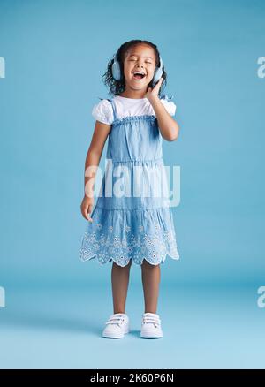 Une adorable petite fille hispanique chante avec les yeux fermés tout en écoutant de la musique avec des écouteurs sans fil appréciant son préféré Banque D'Images