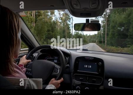 Femme conduisant, vue depuis le siège arrière à un angle bas par rapport au tableau de bord principal de la voiture. Depuis le plan de transport du siège arrière du passager. Banque D'Images