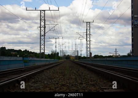 Une piste de train s'étendant sur la distance en milieu de journée avec des lignes électriques au-dessus, bleu, ciel nuageux à l'arrière-plan Banque D'Images