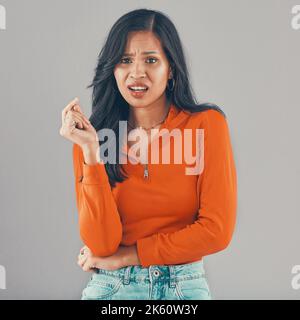 Portrait de la femme de race mixte isolée contre fond gris studio avec espace de copie et l'aspect ennuyé. Jeune hispanique irrité debout seul et Banque D'Images