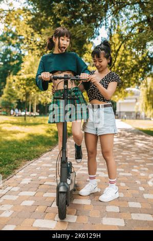 De jolies petites filles élancées qui voyagent en scooter dans le parc Banque D'Images