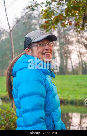 Vue latérale d'une femme souriante portant une casquette de sport et un manteau d'hiver en promenade hivernale dans la campagne britannique. Banque D'Images