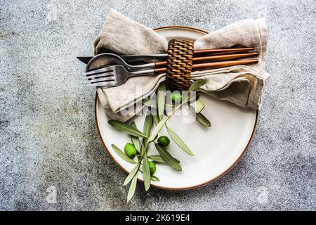 Table d'été rustique avec assiette et couverts décorés de branches d'olivier Banque D'Images