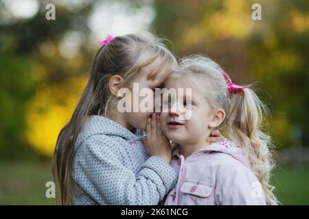 Une petite fille raconte le secret dans l'oreille de son ami. Deux jolies petites filles dans le parc d'automne. Banque D'Images