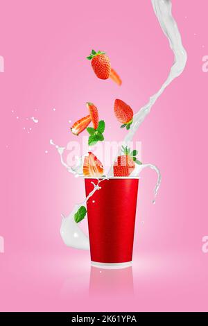 Baies de fraises tombant dans une tasse à emporter en papier avec des éclaboussures de lait. Barbotage au smoothie aux fraises. Banque D'Images