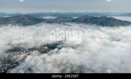 Au-dessus des nuages. Paysage de montagne en couches brumeuses avec une ville dans les Carpates, Ukraine. Banque D'Images