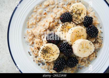 Flocons d'avoine. Bol de porridge de flocons d'avoine avec des graines de mûre, de banane et de chia sur fond de table vieux en béton gris. Vue de dessus en style de pose à plat. Naturel i Banque D'Images