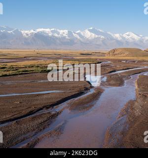 Vue sur le paysage matinale de la rivière Kyzylsu rouge brun avec la chaîne de montagnes Trans Alay enneigée et le pic Lénine en arrière-plan, au sud du Kirghizistan Banque D'Images