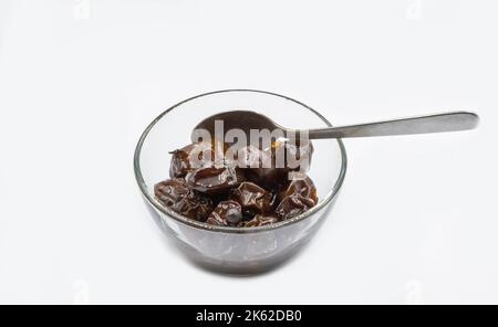 Prunes marinées dans un bol en verre, gros plan sur du blanc Banque D'Images