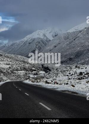 Photo verticale d'une route sinueuse dans les montagnes enneigées des Alpes du Sud de la Nouvelle-Zélande Banque D'Images