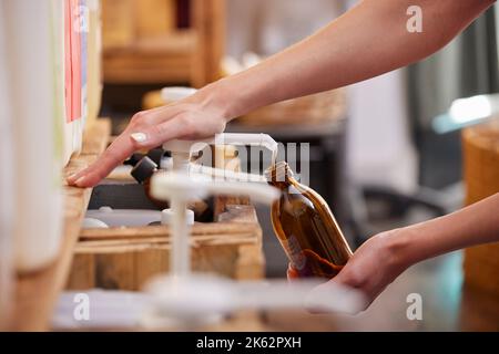 Gros plan de la femme qui recharge une bouteille de verre avec du savon liquide dans un magasin gratuit de plastique zéro déchet durable Banque D'Images