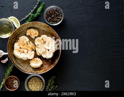 Cuisson du steak de chou-fleur. Le chou-fleur cru parsemé d'épices se trouve dans une poêle à frire. Huile d'olive, herbes, diverses épices à proximité. Arrière-plan sombre. Copie Banque D'Images