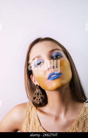 Portrait d'une jolie fille blonde avec un maquillage extrême bleu-jaune; elle porte une robe sans manches Banque D'Images