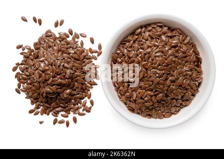 Graines de lin dans un bol en céramique blanc à côté d'une pile de graines de lin isolées sur blanc. Vue de dessus. Banque D'Images