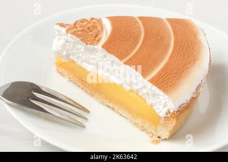 Un morceau de tarte au citron avec garniture meringue sur une assiette blanche à côté d'une fourchette. Banque D'Images