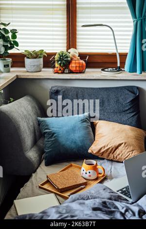 Maison confortable, ambiance chaleureuse à l'automne. Ordinateur portable, carnet et une tasse de thé au plateau sur une couverture dans le lit à l'intérieur de la chambre. Concept d'automne ou d'hiver confortable. Banque D'Images