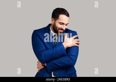 Je suis égoïste, j'aime moi-même. Portrait de l'homme barbu narcissique égoïste s'embrassant et souriant avec une expression satisfaite rêveuse. Prise de vue en studio isolée sur fond gris. Banque D'Images