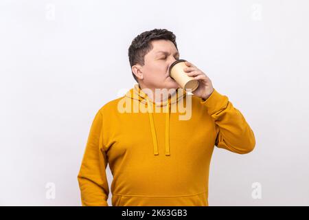 Portrait d'un beau homme d'âge moyen debout et buvant un café à emporter dans une tasse en papier, style de vie frais, port de sweat à capuche de style urbain. Studio d'intérieur isolé sur fond blanc. Banque D'Images