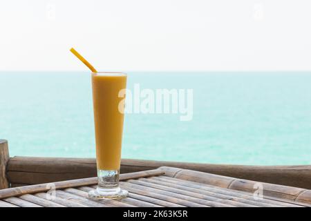 Verre de jus de mangue sur une table en bambou donnant sur la mer. Vacances exotiques, concept de boisson de détente Banque D'Images