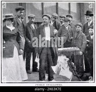 Un homme qui ne cesse jamais d’attirer une foule dans les rues de Londres, avec sa petite table sur laquelle il se régale de petits objets. Avaler des cailloux, des ongles, du verre cassé et des délices similaires. Banque D'Images