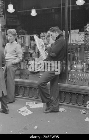 Scène de rue sur 38th Street près de 7th Avenue, New York City. Adolescent lisant le journal. Date 1936 nov Banque D'Images