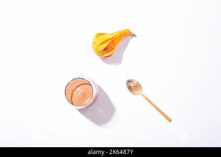 Verre avec smoothie au chocolat avec cuillère et citrouille d'orange sur fond blanc. Concept d'automne. Une alimentation saine. Vue de dessus, plan d'appartement Banque D'Images