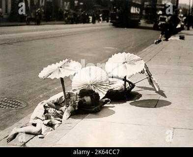 Londres 1920 - une jeune entrereneur s'endort dans le soleil à l'ombre des parasols qu'elle a fait à partir de vieux journaux Banque D'Images