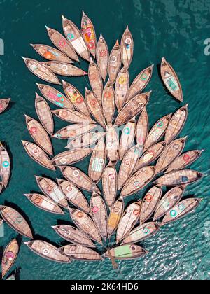 Dhaka, Dhaka, Bangladesh. 11th octobre 2022. Une flotte de bateaux en bois, qui ressemblent aux pétales de fleurs, attend de faire des traversiers sur le fleuve Buriganga pour trouver des emplois dans un port majeur de Dhaka, au Bangladesh, tandis que les bateaux se marient les uns avec les autres dans un modèle fleuri et obtiennent quarante clins d'œil avant l'heure de pointe de l'après-midi. Ils travaillent 16 heures par jour et obtiennent moins de 5 £ pour cela. Ainsi, ils prennent le repos chaque fois qu'ils ont une chance de soulager la fatigue des longues heures de travail. Pendant ce temps, la plupart des bateaux sont reliés ensemble, sauf quelques-uns, et le nombre de passagers est inférieur à t Banque D'Images