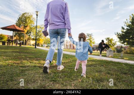 vue arrière de la mère et de l'enfant inconnus femme et fille fille femelle marchant dans le parc tout en tenant les mains adulte et 18 mois de maternité et de la maternité Banque D'Images