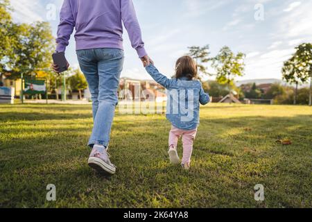 vue arrière de la mère et de l'enfant inconnus femme et fille fille femelle marchant dans le parc tout en tenant les mains adulte et 18 mois de maternité et de la maternité Banque D'Images