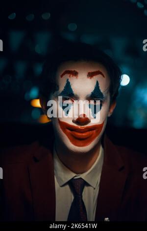 Guy en costume et cravate avec le maquillage Joker regarde la caméra. Banque D'Images