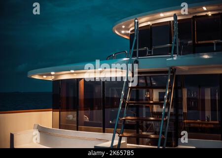 Un cliché nocturne d'un luxueux pont de bateaux de plongée avec plusieurs plafonniers, avec une échelle à l'avant et une rangée de fenêtres en verre avec une salle Banque D'Images