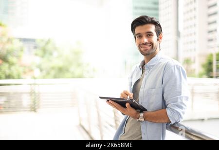 Le jeune homme utilise une tablette pour s'entraîner à l'extérieur du bureau. L'homme portant un tissu décontracté et se sentant détendu et heureux. Banque D'Images