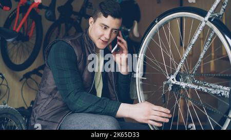 Sérieux jeune homme professionnel de vélo réparateur vérifie et tourne le volant tout en parlant sur téléphone portable. Entretien de bicyclettes, communication et concept de profession. Banque D'Images