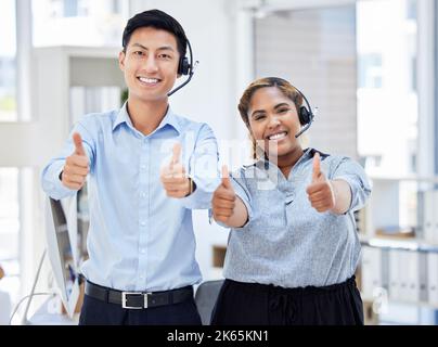 Deux jeunes hommes et femmes heureux agents de centre d'appels montrant le pouce vers le haut tout en répondant aux appels travaillant dans un bureau au travail. Heureux asiatique homme et mélangé Banque D'Images