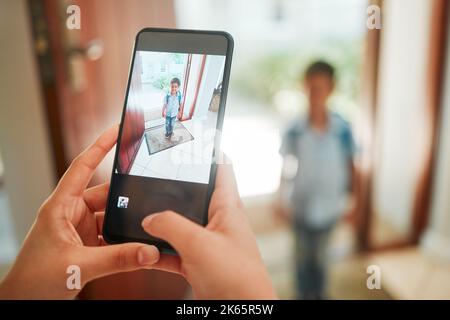 Gros plan de la mère prenant la photo de son fils le premier jour de l'école. Mains prenant la photo sur le téléphone portable de garçon de jardin d'enfants debout près de la porte et prêt à Banque D'Images