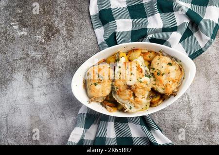 Cabillaud cuit avec des pommes de terre et des herbes dans un plat blanc sur fond gris foncé. Vue de dessus, plan d'appartement Banque D'Images