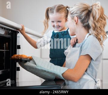 La mère tient un plateau de muffins. Bonne femme prenant un plateau de muffins frais et cuits au four. Petite fille qui cuit avec sa mère. Mère et fille Banque D'Images